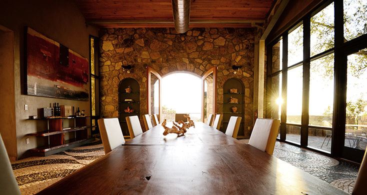 long wood table with padded chairs and a stone wall in the background